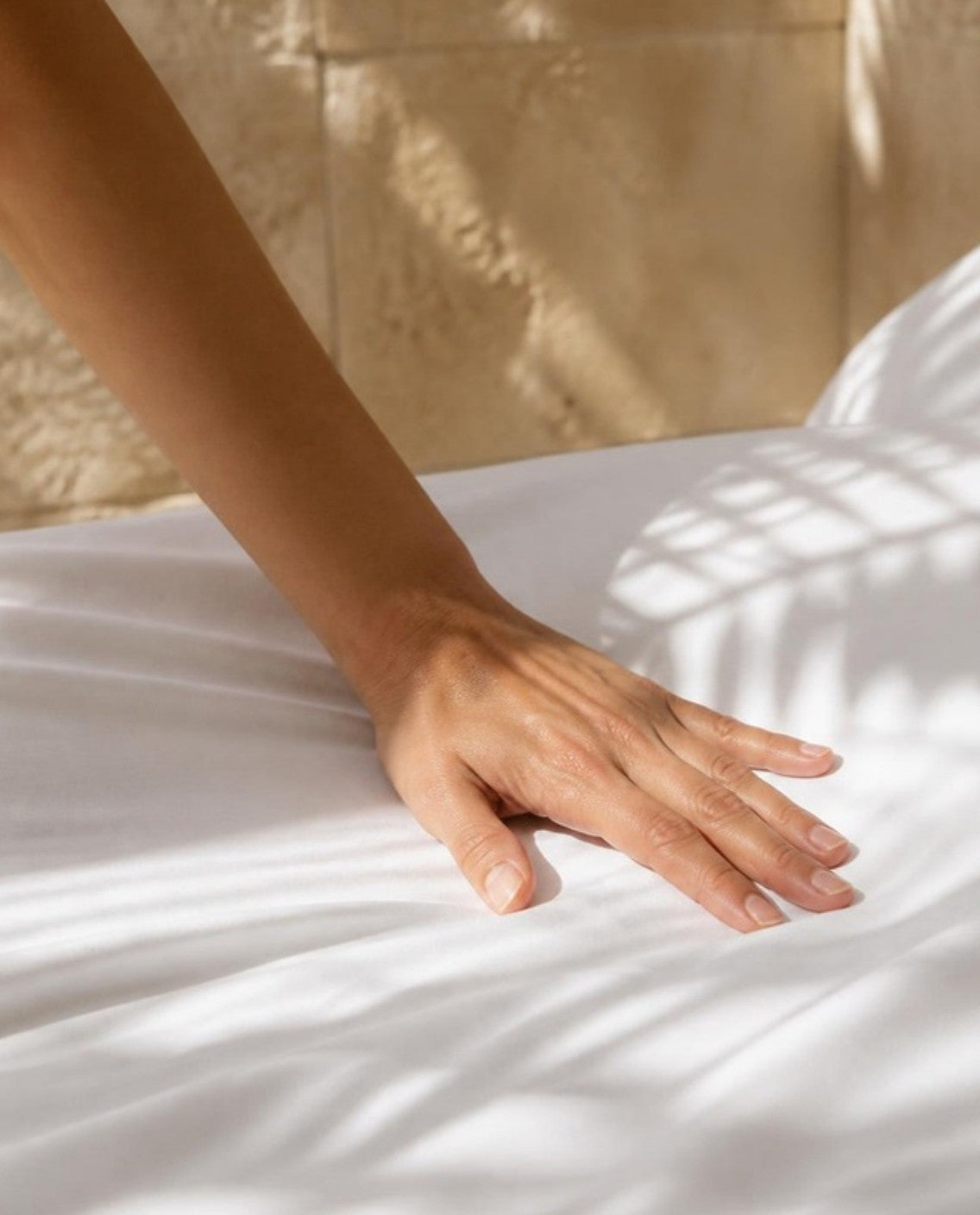 Hand streicht über glatte weiße Satin-Bettwäsche aus ägyptischer Baumwolle im Morgenlicht